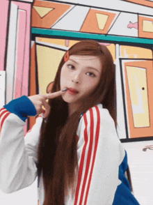a woman with long hair and red white and blue stripes on her jacket looks at the camera