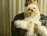 a man with glasses is holding a small white dog in his arms