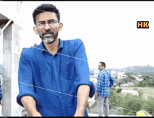 a man with glasses and a beard is standing in front of a sign that says " hk "