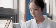a woman in a white robe is looking at her cell phone .