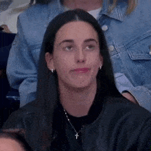 a woman wearing a black leather jacket and a cross necklace is sitting in a crowd .