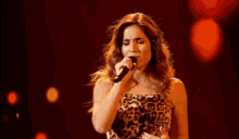a woman in a leopard print dress is singing into a microphone on a stage .