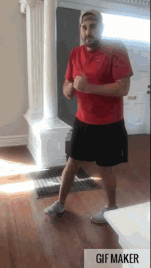 a man in a red shirt and black shorts is standing in a living room with a gif maker icon below him