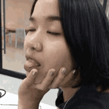 a woman with a nose ring is sticking her tongue out while holding her hand to her face .