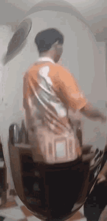 a man in an orange shirt is standing in front of a mirror looking at himself .