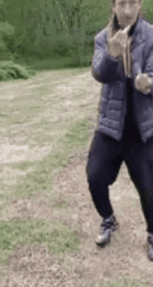 a man in a blue jacket is standing on a dirt road holding a rope .