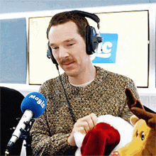 a man wearing headphones is holding a stuffed animal in front of a microphone that says magic