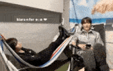 a man is laying in a hammock next to another man who is sitting in a chair .