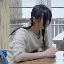 a girl with braids is sitting at a table with her hands folded
