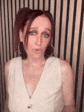 a woman with red hair is wearing hoop earrings and a white vest .