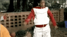 a young man in a red and white jacket is dancing in front of a brick wall .