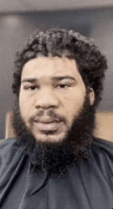 a man with a beard is wearing a black cape .