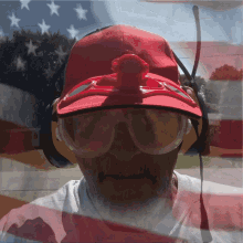 a man wearing a red hat and headphones stands in front of an american flag