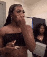 a woman in a black crop top is applying makeup to her face