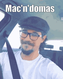 a man wearing glasses and a hat is sitting in a car with the words mac ' n ' domas written above him