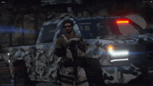a man standing in front of a camo truck with a blue light on