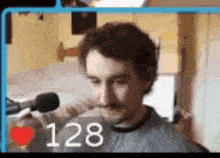 a man is sitting in front of a microphone with the number 128 on the bottom right .