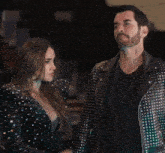 a man in a studded leather jacket stands next to a woman in a sequined dress