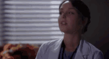 a woman in a lab coat is sitting in front of a window and looking up .
