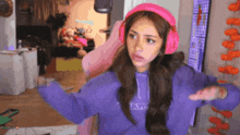 a girl wearing pink headphones and a purple sweatshirt is dancing in a room .