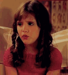 a young girl with braids is sitting on a couch making a funny face .