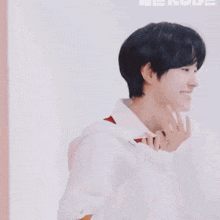 a young man wearing a white hoodie and a red shirt is smiling and making a heart with his hands .