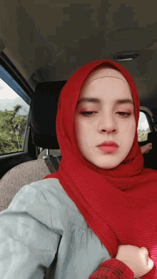 a woman wearing a red hijab sits in a car with her eyes closed