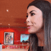 a woman is sitting in front of a red wall with a framed picture on it