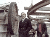a man in a suit and tie is standing in front of a large wheel