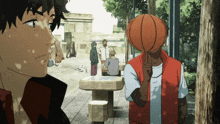 a man with a basketball on his head stands in a park with other people