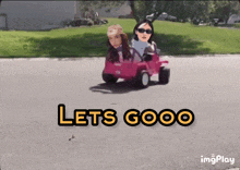 two women are driving a pink toy car with the words let 's gooo written on the bottom