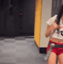 a woman in a white crop top and red shorts is standing in a gym holding a bottle of water .