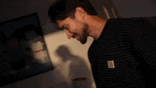 a man with a beard is laughing in front of a painting on a wall .