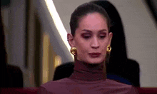 a woman wearing a turtleneck and gold earrings is sitting in a theatre .