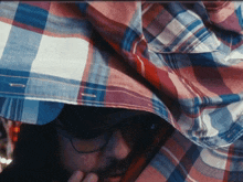 a man wearing sunglasses and a plaid shirt is covering his face