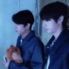 two men in blue jackets are standing next to each other one is holding a stuffed animal
