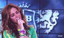 a woman singing into a microphone in front of a wall with the letter b on it