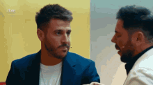 a man in a suit talks to another man in front of a yellow wall with the letters rtve on the bottom