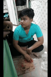 a boy in a blue shirt sits on the floor with a bottle of water in front of him
