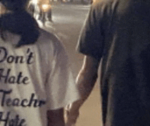 a man and a woman are holding hands while walking down a street at night .