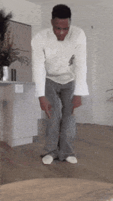a man in a white shirt and grey pants is standing on a wooden floor