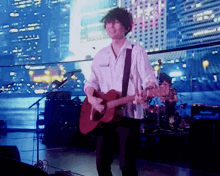 a man in a white shirt is playing a guitar on a stage