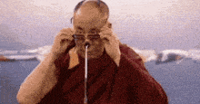 a man in a red robe is adjusting his glasses while holding a microphone in his mouth .