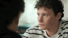 a man in a striped shirt is looking at another man 's face
