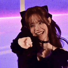 a young woman wearing a choker and cat ears is pointing at the camera .