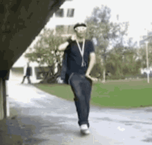 a man wearing sunglasses and a lanyard around his neck is walking down a sidewalk .