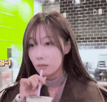a woman drinking through a straw with a brick wall behind her
