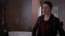 a woman in a leather jacket and a red shirt is standing in a bathroom .