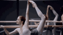 a woman in pointe shoes stretches her leg over a bar