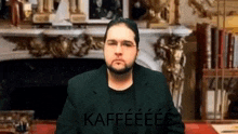 a man with glasses and a beard is sitting in front of a fireplace with the word kaffeeeee written on the screen